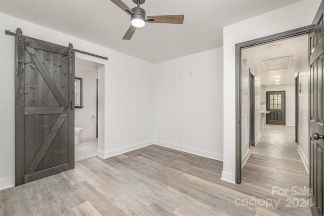 unfurnished room featuring ceiling fan, a barn door, and light wood-type flooring