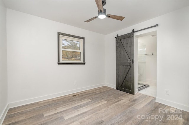 unfurnished bedroom with a barn door, ensuite bathroom, light hardwood / wood-style flooring, and ceiling fan