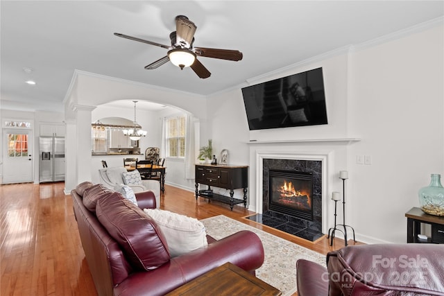 living room with a tile fireplace, ceiling fan with notable chandelier, decorative columns, light hardwood / wood-style floors, and crown molding