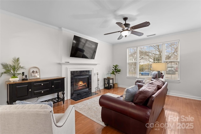 living room featuring ornamental molding, ceiling fan, a high end fireplace, and light hardwood / wood-style floors