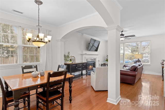 dining space with ornate columns, crown molding, ceiling fan with notable chandelier, and light hardwood / wood-style floors