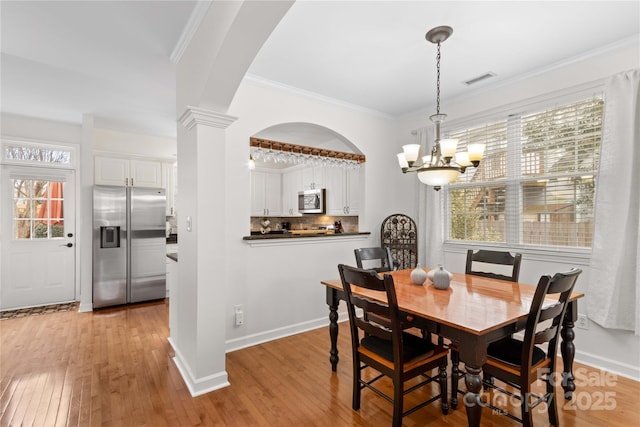 dining area with ornate columns, crown molding, an inviting chandelier, and light wood-type flooring