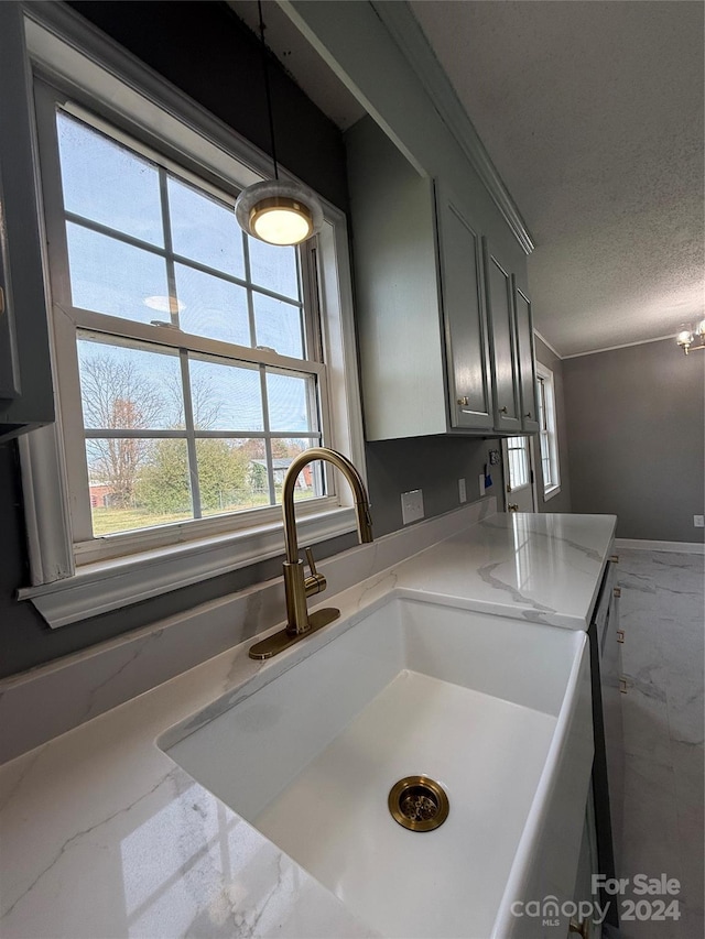 kitchen with sink, hanging light fixtures, crown molding, a textured ceiling, and gray cabinets