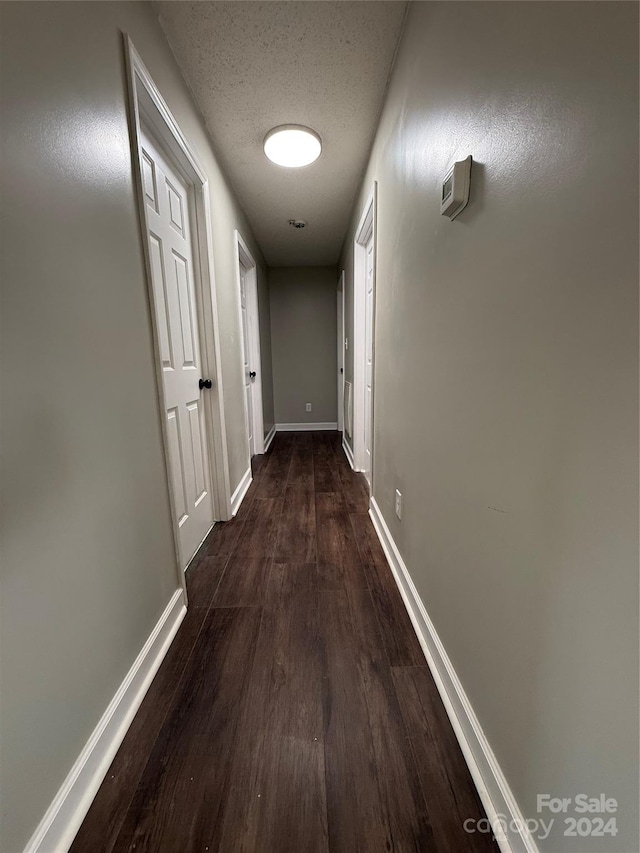 hall with a textured ceiling and dark wood-type flooring