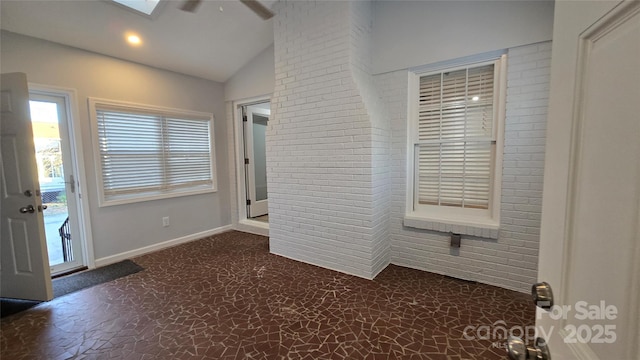 interior space featuring brick wall, access to outside, vaulted ceiling with skylight, and ceiling fan