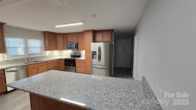 kitchen featuring appliances with stainless steel finishes, light stone counters, a peninsula, light wood-type flooring, and a sink