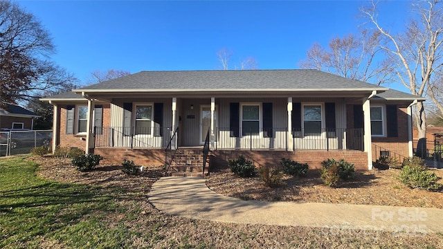 view of front of home with covered porch, brick siding, roof with shingles, and fence