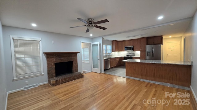 kitchen featuring visible vents, appliances with stainless steel finishes, a brick fireplace, light wood-type flooring, and a peninsula