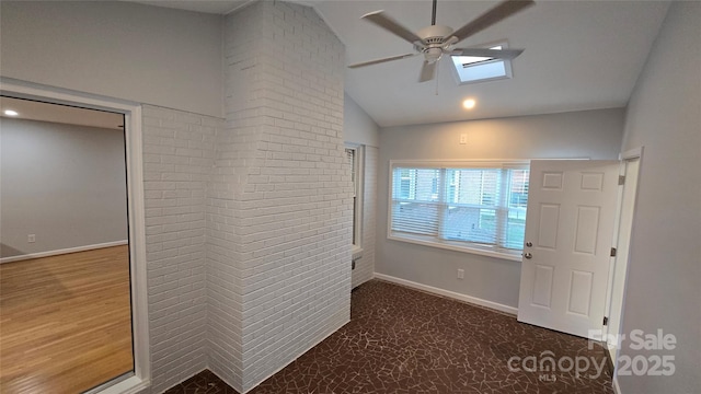 empty room with carpet floors, vaulted ceiling, ceiling fan, brick wall, and baseboards