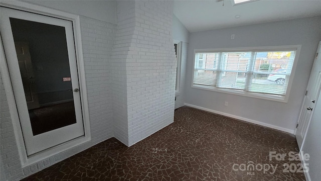 unfurnished room with lofted ceiling, brick wall, and baseboards