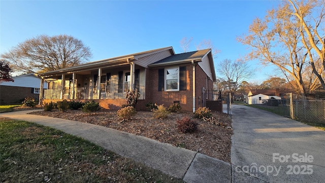 view of front facade with covered porch, driveway, brick siding, and fence