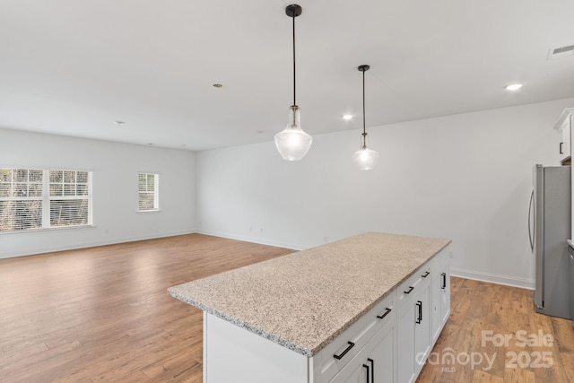 kitchen with white cabinetry, pendant lighting, stainless steel refrigerator, and a kitchen island