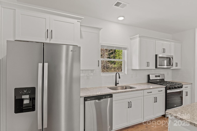 kitchen featuring sink, white cabinetry, stainless steel appliances, light stone countertops, and decorative backsplash