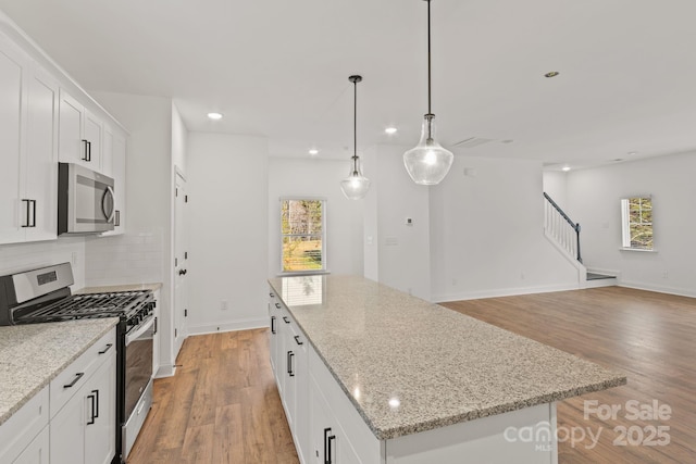 kitchen featuring stainless steel appliances, light stone countertops, a center island, and white cabinets