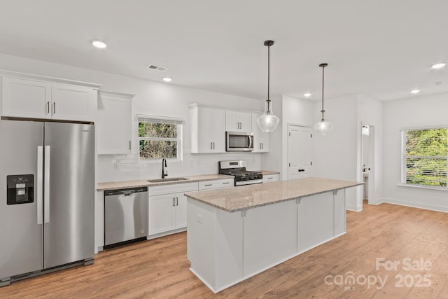 kitchen featuring sink, white cabinets, hanging light fixtures, a center island, and stainless steel appliances