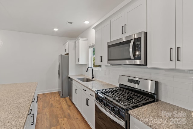 kitchen featuring sink, white cabinets, stainless steel appliances, light stone countertops, and light wood-type flooring