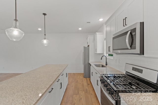 kitchen with sink, appliances with stainless steel finishes, hanging light fixtures, light stone counters, and white cabinets