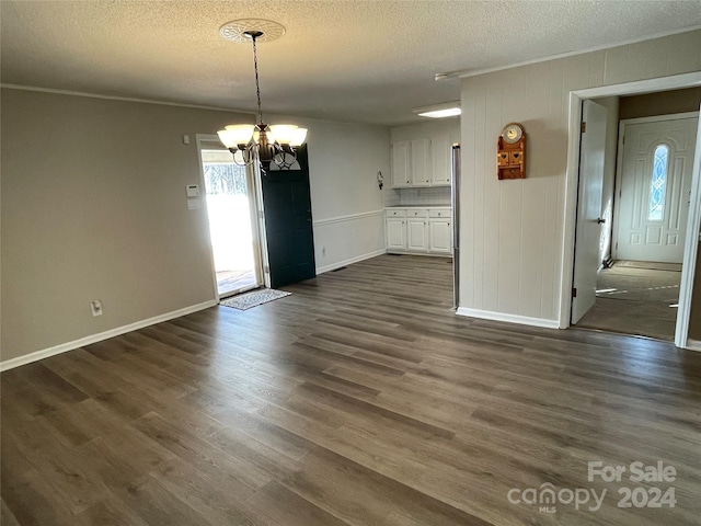 unfurnished dining area featuring dark hardwood / wood-style floors, ornamental molding, a textured ceiling, and an inviting chandelier