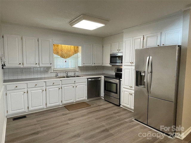 kitchen featuring decorative backsplash, appliances with stainless steel finishes, sink, light hardwood / wood-style flooring, and white cabinets