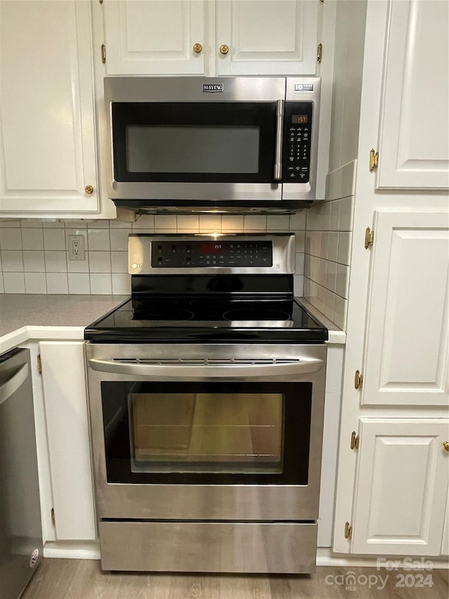 kitchen with white cabinets, backsplash, stainless steel appliances, and light hardwood / wood-style floors