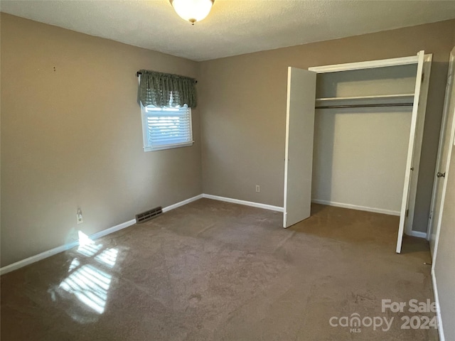 unfurnished bedroom with a textured ceiling, carpet floors, and a closet