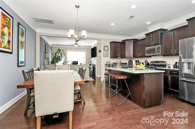 kitchen with a breakfast bar, dark hardwood / wood-style floors, an island with sink, dark brown cabinets, and appliances with stainless steel finishes