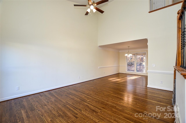 unfurnished living room featuring dark hardwood / wood-style floors, ceiling fan with notable chandelier, crown molding, and a high ceiling