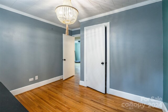 unfurnished bedroom with crown molding, wood-type flooring, and an inviting chandelier