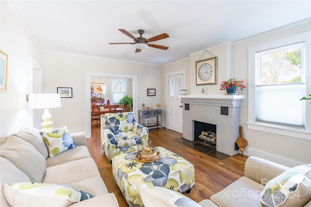 living room with ceiling fan, crown molding, dark hardwood / wood-style floors, and a brick fireplace