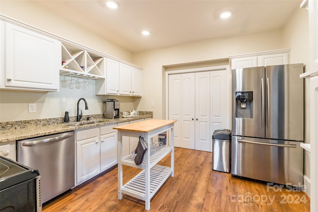 kitchen featuring light stone countertops, white cabinets, stainless steel appliances, and hardwood / wood-style flooring