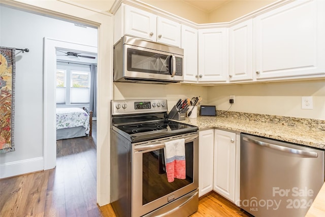 kitchen with light stone countertops, stainless steel appliances, ceiling fan, light hardwood / wood-style flooring, and white cabinetry