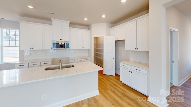 9601 Pointer Rd Unit 77, Huntersville, NC 28078 - kitchen with sink, light hardwood / wood-style flooring, light stone countertops, a kitchen island with sink, and white cabinets
