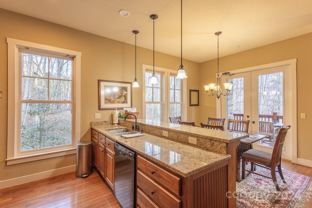 kitchen featuring light stone countertops, sink, black dishwasher, decorative light fixtures, and a breakfast bar area