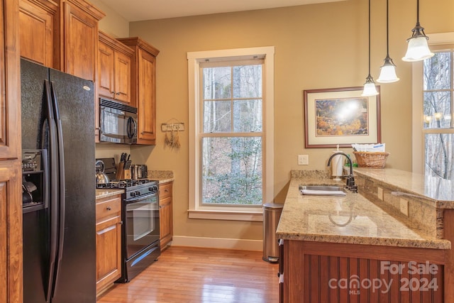 kitchen with sink, light stone counters, kitchen peninsula, pendant lighting, and black appliances