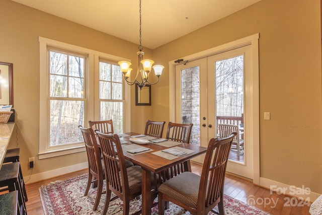 dining room with french doors, light wood-type flooring, a healthy amount of sunlight, and a notable chandelier