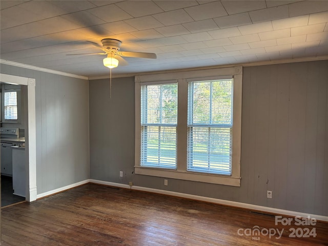 empty room featuring wooden walls, dark hardwood / wood-style floors, ceiling fan, and ornamental molding