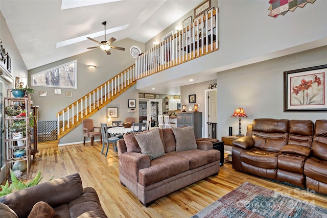 living room with ceiling fan, a skylight, high vaulted ceiling, and light hardwood / wood-style flooring