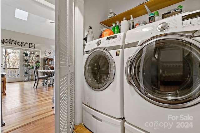 laundry room with washing machine and clothes dryer, a skylight, and hardwood / wood-style flooring