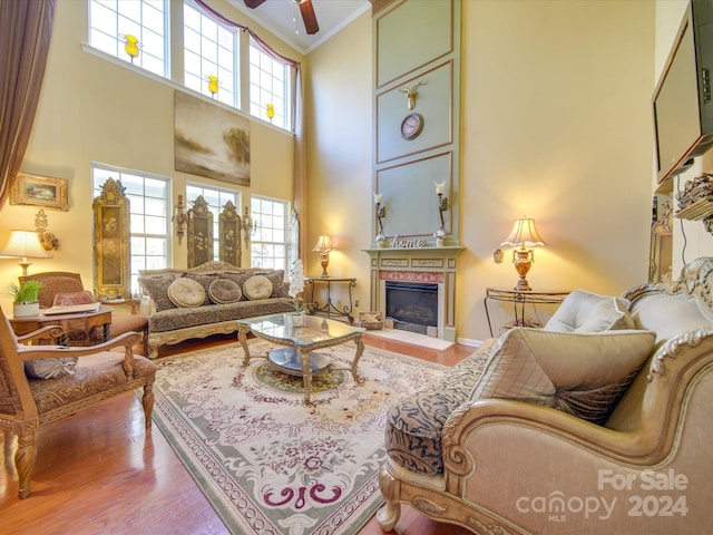 living room featuring ceiling fan, crown molding, a towering ceiling, and wood-type flooring