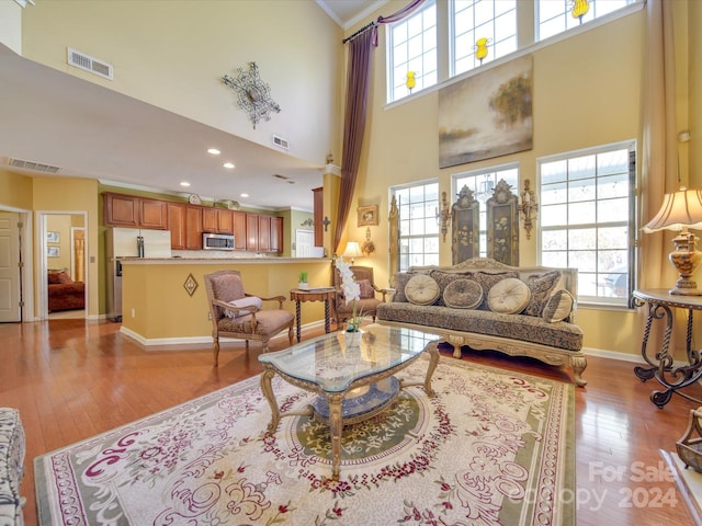 living room featuring a towering ceiling, light hardwood / wood-style floors, a wealth of natural light, and crown molding