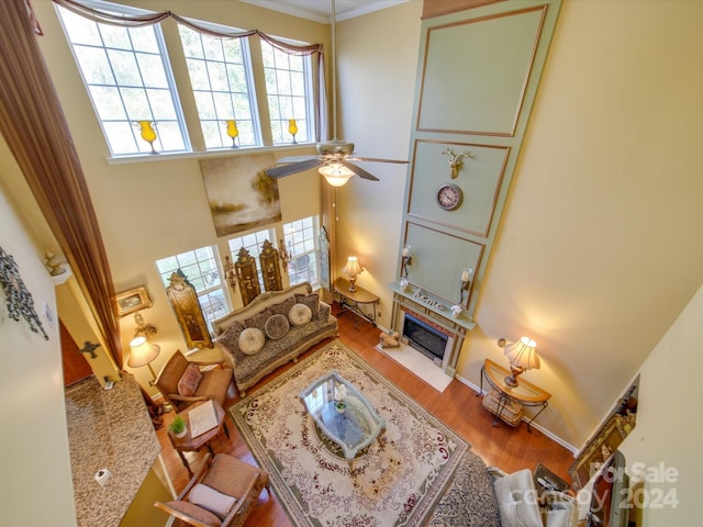 living room featuring a high end fireplace, hardwood / wood-style flooring, ceiling fan, ornamental molding, and a towering ceiling