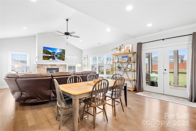 dining space with lofted ceiling, a stone fireplace, light wood-type flooring, and french doors