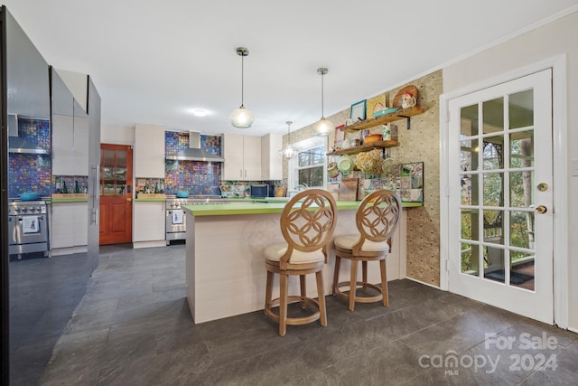 kitchen with kitchen peninsula, a wealth of natural light, stainless steel range, and wall chimney exhaust hood