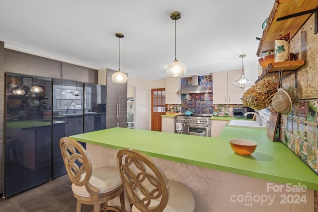 kitchen featuring double oven range, wall chimney range hood, sink, tasteful backsplash, and kitchen peninsula