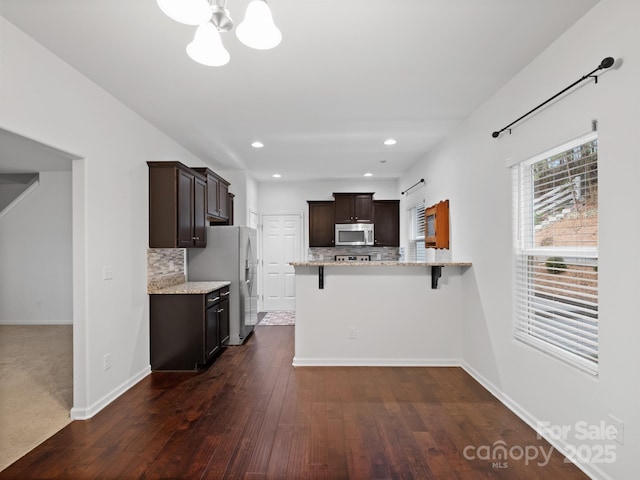 kitchen with a breakfast bar area, appliances with stainless steel finishes, dark hardwood / wood-style flooring, decorative backsplash, and kitchen peninsula