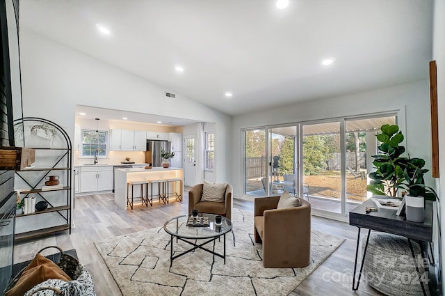 living room with light hardwood / wood-style floors, high vaulted ceiling, and sink