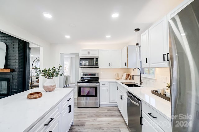 kitchen featuring white cabinets, sink, appliances with stainless steel finishes, decorative light fixtures, and light hardwood / wood-style floors