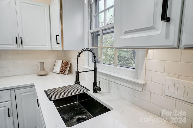 interior details featuring light stone countertops, white cabinetry, sink, and tasteful backsplash