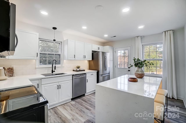 kitchen featuring sink, stainless steel appliances, light hardwood / wood-style flooring, pendant lighting, and white cabinets