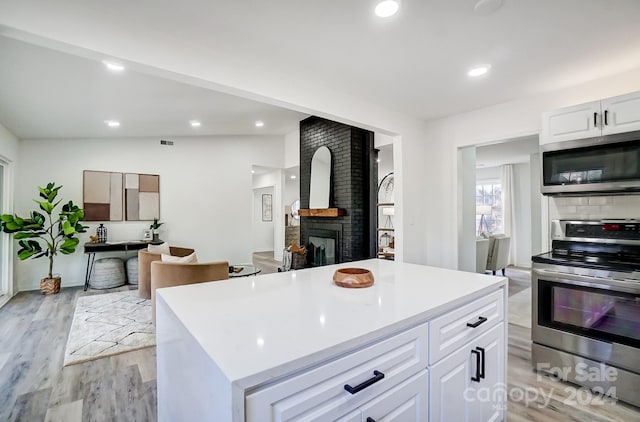 kitchen with a center island, lofted ceiling, a brick fireplace, appliances with stainless steel finishes, and white cabinetry